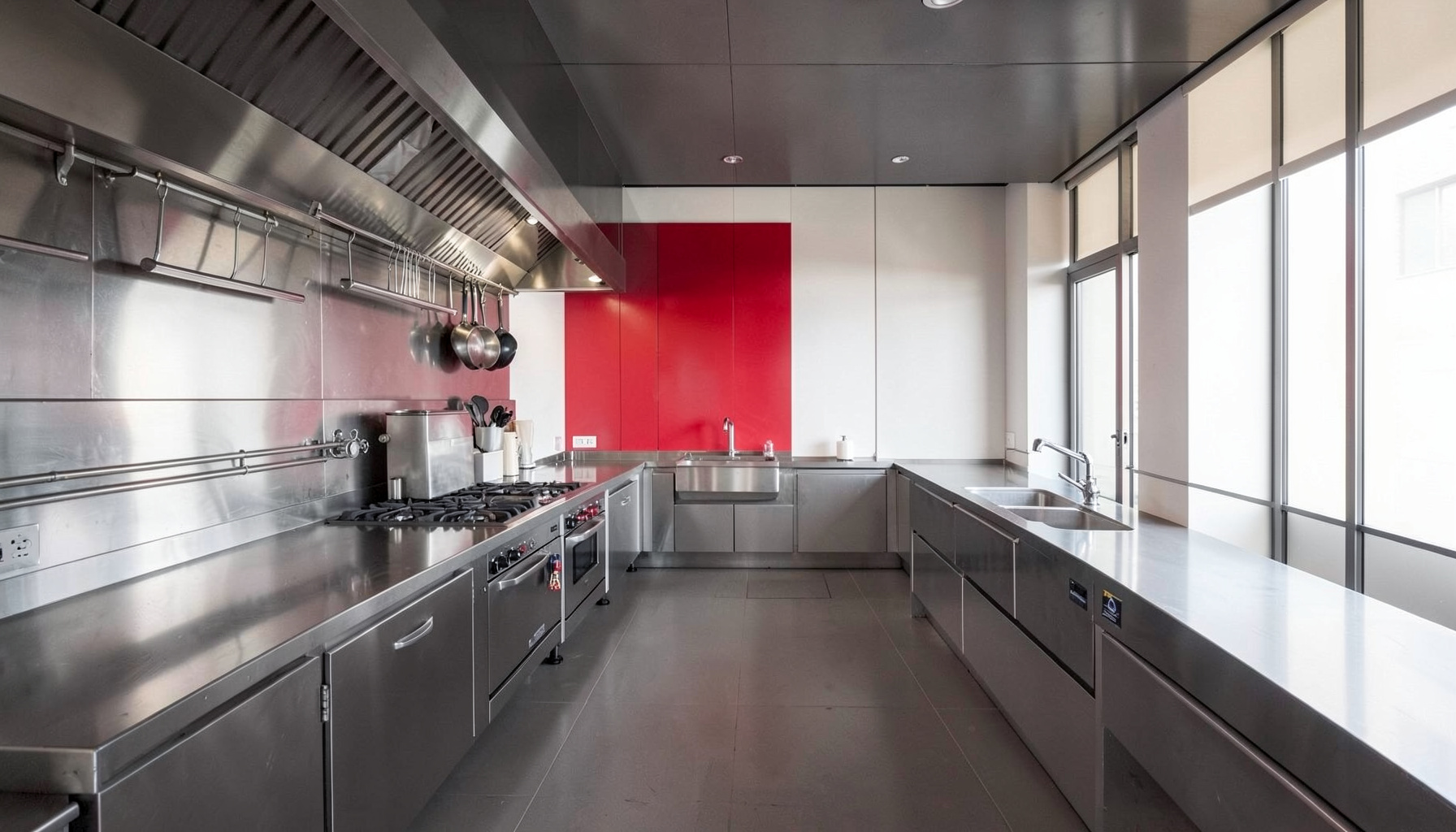 Cocina profesional con encimeras de acero, utensilios ordenados y luz natural que entra por un ventanal.