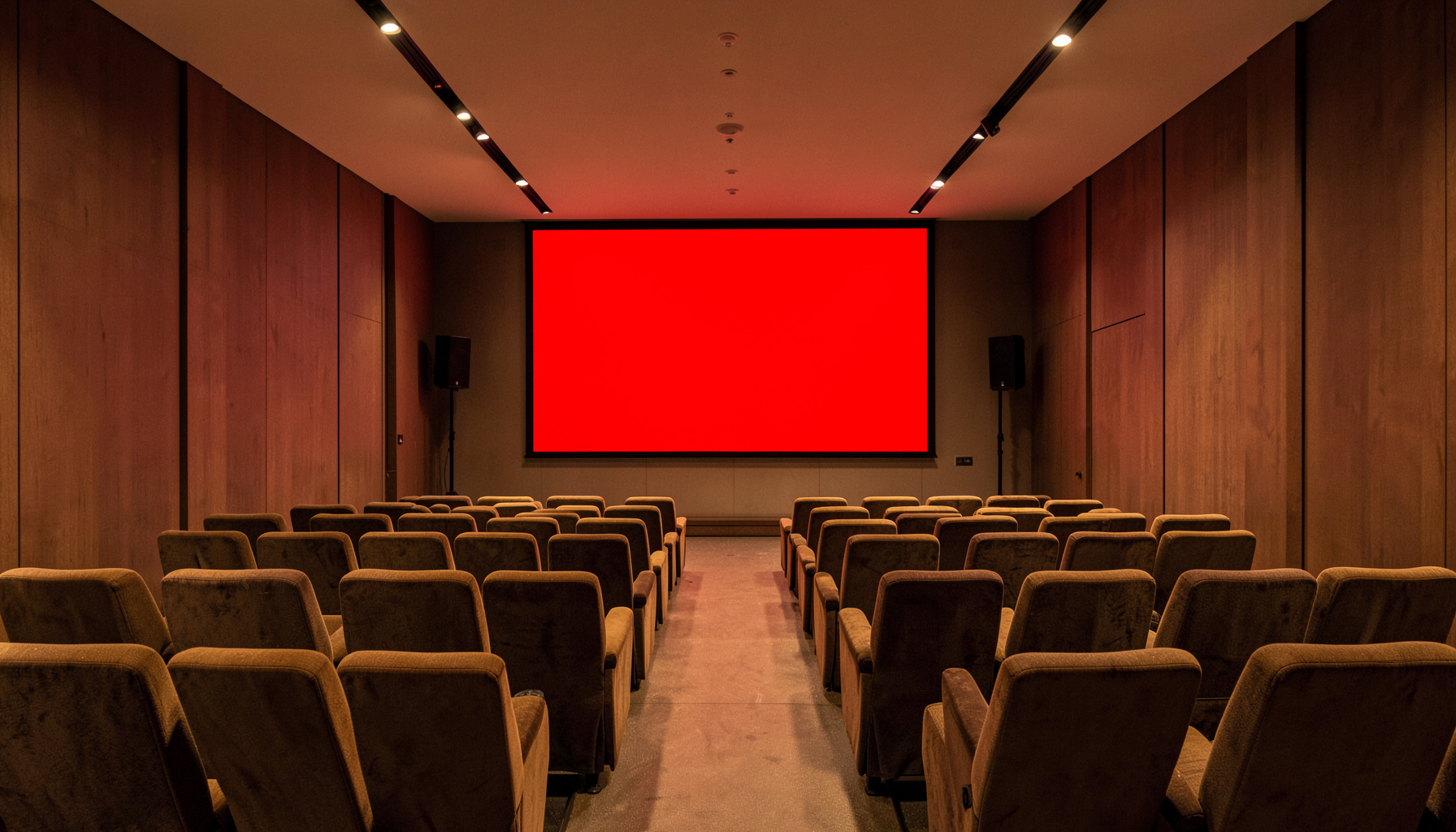 Sala de conferencias con butacas tapizadas en tonos tierra, iluminación cálida y una pantalla de proyección.