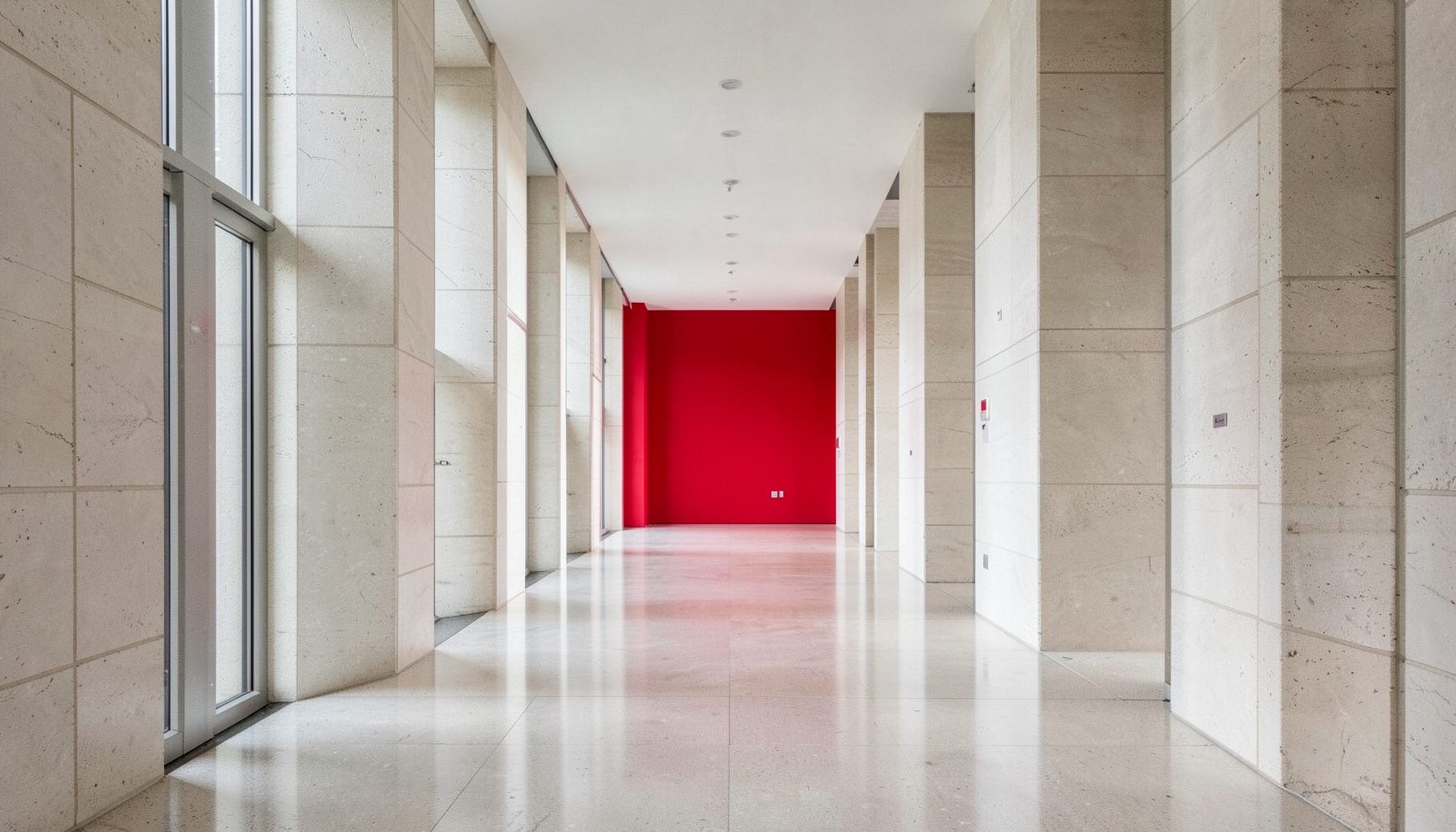 Pasillo simétrico de un edificio institucional moderno, con columnas de piedra clara, suelo pulido y luz natural difusa que transmite serenidad y exclusividad.