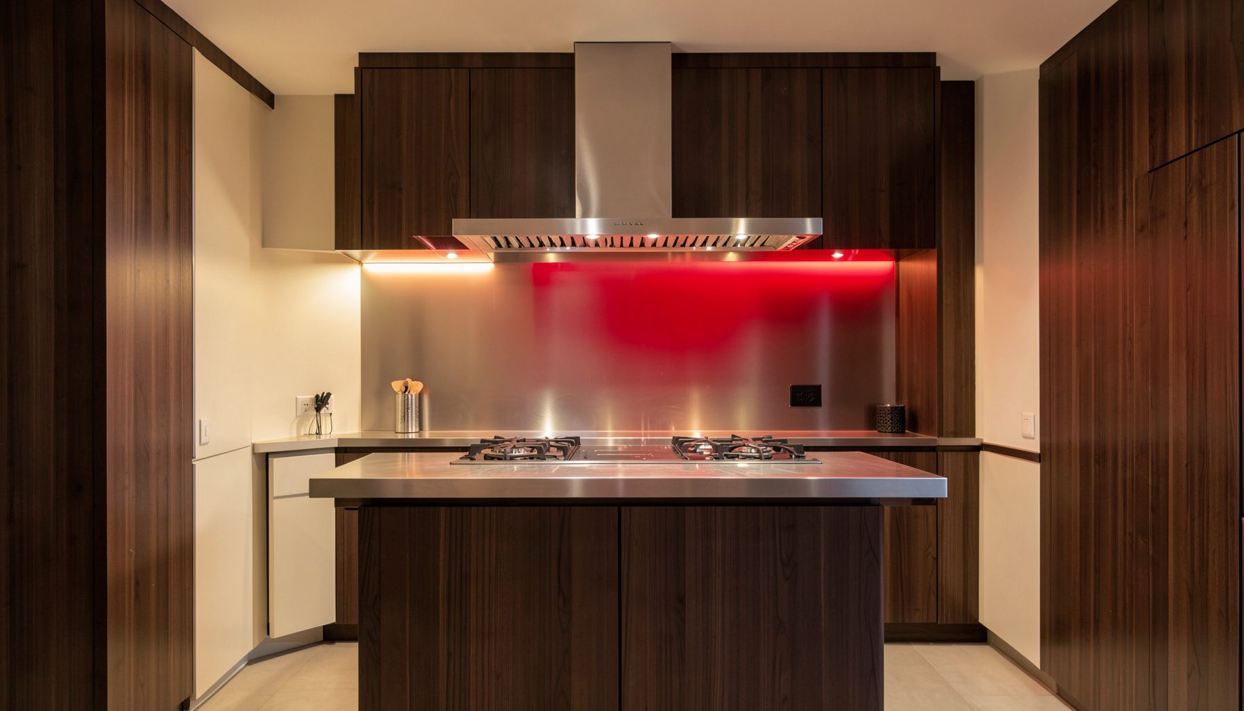 Cocina profesional con encimera de acero inoxidable, iluminación cálida y ambiente sereno, en tonos crema y madera oscura.