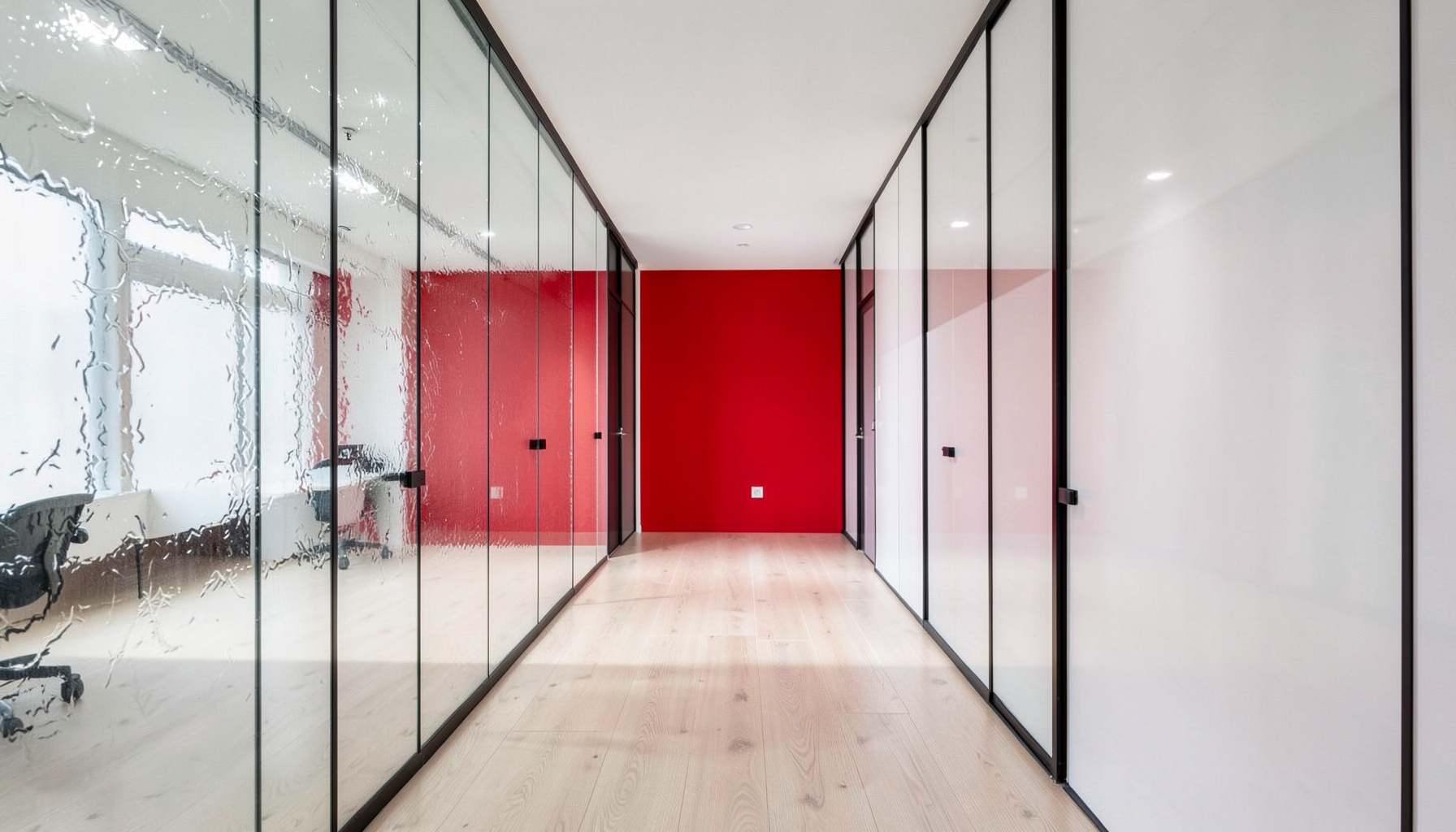Pasillo de oficina contemporánea con paredes de cristal esmerilado, suelo de madera clara y luz natural difusa que transmite serenidad y profesionalidad.